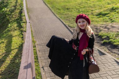Bir kız bordo palet ve biet ile merdivenlerden yukarı çıkar, siyah giysiler içinde, sonbaharda bir gölün arka planında mavi bulutlar vardır..