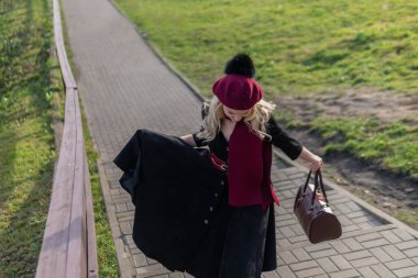 Bayan merdivenlerden yukarı çıkar ve bordo palet ve biet ile, siyah elbiseli bir yetişkin, mavi gökyüzü arka planına karşı sonbaharda kameraya bakar..