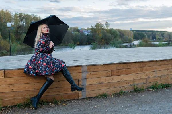 Žena s tmavým deštníkem sedí na dřevěném schodišti v pozadí nadýchaného mraku na jevišti. s charismatickým vzhledem — Stock fotografie