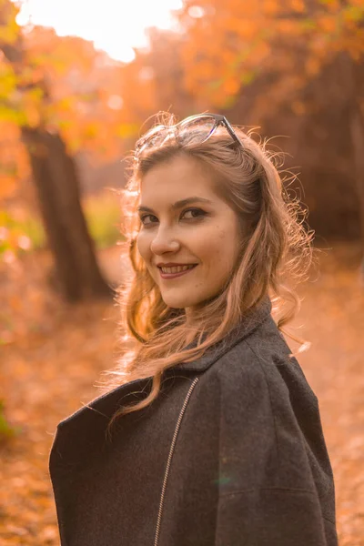 Een vrolijk meisje in een zwarte mantel draagt kameleon glazen in de herfst. Geel bos, groen gras, blond. met zachte lippen — Stockfoto