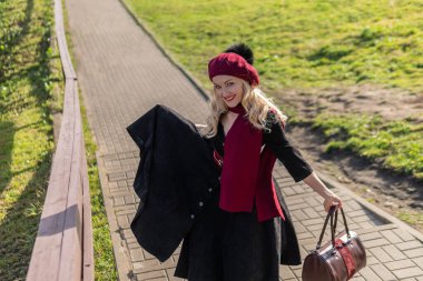 Mutlu bir kadın bordo palet ve biet ile merdivenlerden yukarı çıkar, siyah elbiseli güzel gözleri olan bir yetişkin, sonbaharda ağaçların arka planında mavi bulutların karşısında..