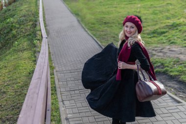 Mutlu bir kadın bordo palet ve biet ile merdivenlerden yukarı çıkar, siyah elbiseli güzel bir gülümsemesi olan bir yetişkin, sonbaharda ağaçların arka planında mavi bulutlara karşı..