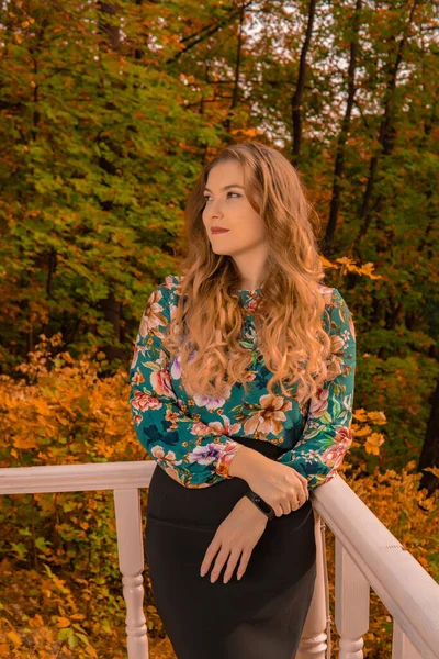 Um adolescente alegre está inclinado contra um corrimão branco uma jovem loira, em uma camisa colorida fica contra um fundo do lago rindo outono perfeito abraçar olhos azuis — Fotografia de Stock