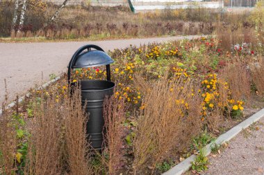 Şehir parkındaki bir çöp tenekesi, taştan yapılmış bir yolun yakınındaki çimenlikte metalden yapılmış bir çöp tenekesi, güneşli havalarda konseptin tadını çıkar.