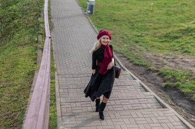 Mutlu bir kız merdivenlerden yukarı çıkar ve bordo pist ve biet ile, siyah elbiseli güzel gözleriyle, sonbaharda bir göletin arka planında, mavi bulutların üzerinde yürür..