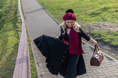 Bir kadın merdivenlerden yukarı çıkıyor ve bordo palet ve biet ile, siyah elbiseli kameraya bakıyor, sonbaharda mavi bulutların arka planına bakıyor..