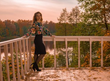 Neşeli bir kadın beyaz korkuluklara yaslanmış renkli tişörtlü, karizmatik görünümlü bir yetişkine yaslanmış göldeki entelektüel sonbahar koleji bilgisayarının arka planında çalışıyor.