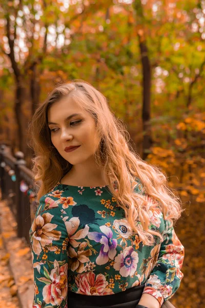 Radostná žena stojí opřená o bílé zábradlí s jemnými rty blondýny v barevné košili, stojí na pozadí schodů humorného podzimního salonu — Stock fotografie