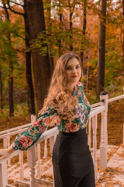 Gülümseyen bir sarışın beyaz bir korkuluğa yaslanır nazik dudakları olan bir yetişkine sarılır, renkli bir gömleği olan bir sarışına, arka planda durur.