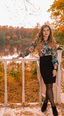 Neşeli bir sarışın, beyaz bir korkuluğa yaslanmış, renkli gömlekli güzel gözleri olan, basamaklarda olumlu duyguları olan, sonbahar saç kesimi yapan, klasik mavi gözlü.