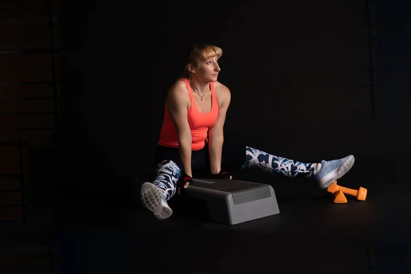 Paso aeróbicos sobre un fondo oscuro se para en sus manos con mancuernas en ropa brillante, en la plataforma mancuernas de color naranja de una mujer turca — Foto de Stock