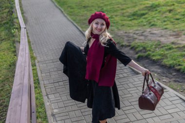 Neşeli bir kadın bordo palla ve biret 'le merdivenlerden yukarı çıkıyor. Mavi gökyüzüne karşı düşerken siyah giysiler içinde karizmatik bir görünüşü olan bir yetişkin. Geniş etek ve el çantası.