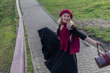 Merry merdivenlerden yukarı çıkar ve bordo palet ve biet ile, siyah elbiseli karizmatik bir yetişkin, bir ağacın arka planına karşı sonbaharda