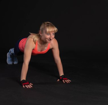 Halterli halterli bir platformda spor yapmak. Siyah arka planda spor yapmak için içeri giriyorlar. Yumuşak dudaklarla gülümsüyorlar. egzersiz tahtası