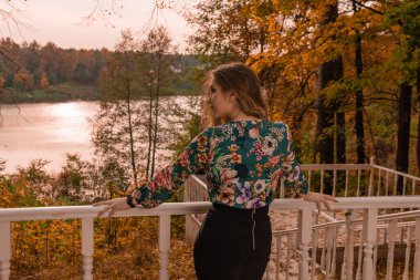 Neşeli gençlik beyaz korkuluklara yaslanmış renkli gömlekli güzel gözleri olan genç bir sarışının önünde duruyor. Arka planda, sonbaharın şehvetli, parlak mavi gözleri var.