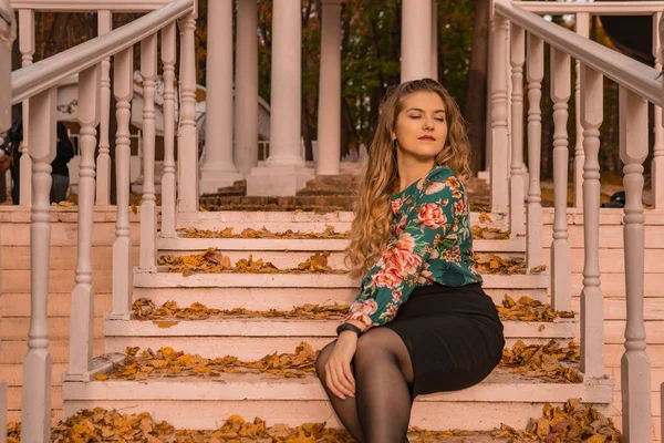 Feliz adolescente se para mirando a la cámara rubia en una camisa de color, teniendo, en el fondo de los pasos, hacer un abrazo de otoño — Foto de Stock