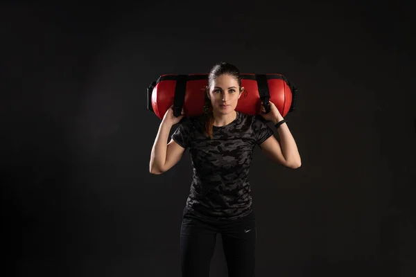 Mulher fitness com Aqua Bag, fica nos ombros de uma bolsa. Esportes em um fundo preto Sorrindo olha para a câmera — Fotografia de Stock