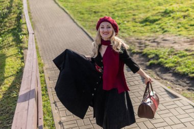 Güzel bir bayan merdivenlerden yukarı çıkıyor ve bordo palet ve biet giyiyor, siyah elbiseli kameraya gülümsüyor, sonbaharda mavi gökyüzü arka planına karşı..