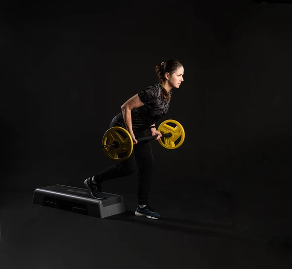 Fitness em uma plataforma de passo, com uma barra, panquecas amarelas no bar fica em um rack. Indo para esportes em um fundo preto Aparência carismática sorridente — Fotografia de Stock