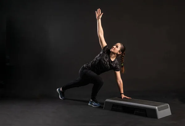 Chica de fitness en el paso en una plataforma de mano, haciendo ejercicios. Participar en deportes sobre un fondo negro Feliz mirando a la cámara — Foto de Stock