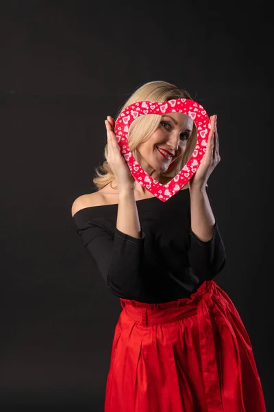 Menina segurando um coração no nível dos olhos vermelho, flertando, no casamento corações chão. banner de inspiração. fórmula do amor do amor, preto no vestido vermelho menina, descalço — Fotografia de Stock