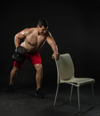 Elinde sandalyesi olan bir adam çıplak bedenini sallıyor. Genç erkek yetişkin model, yaşam tarzı özgüven formda. Stüdyo resmi, başarılı gülüş arka plan siyah vücut geliştirici