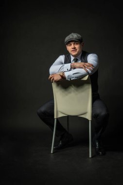 Kafkasyalı, sandalyede duran genç bir erkek, üç parçalı beyaz bir model, sıradan bir yaşam tarzı. Stüdyo başarı şıklığı arka plan siyah vücut geliştirici