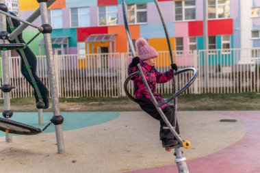 Oyun parkında dönen bir pipoyla oynayan bir kız, eğlence merkezinde kalın bir ceket ve şapka giyiyor, neşeli..