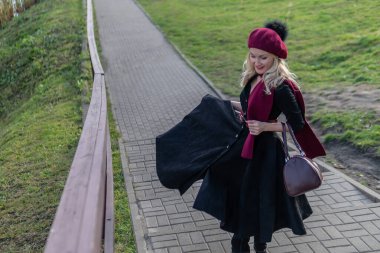 Neşeli bir kız bordo bir palet ve biet ile merdivenlerden yukarı çıkar, siyah giysiler içinde karizmatik bir görünüm ile, sonbaharda ağaçların arkasında mavi bir gökyüzü vardır..