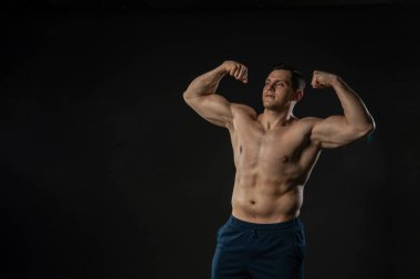 Erkek pazıları çıplak gövde gösteriyor. Kendine güvenen genç erkek, sıradan vücut geliştirici. Güzel moda, dambıl gülüşü arka planda siyah vücut geliştirici