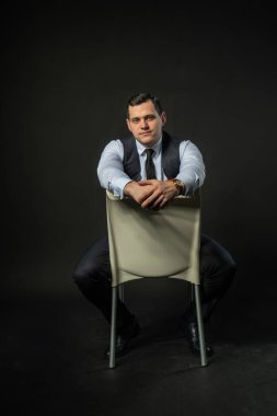 Üç parçalı takım elbise içinde bir sandalyede genç adam üç parçalı takım elbise iş hayatı tarzı erkek kıyafetleri. Siyah vücut geliştirici stüdyo modası, başarılı zarafet arka planı