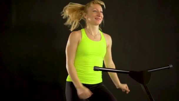 Dziewczyna na trampolinie fitness na czarnym tle w żółtym t-shirt black energy sport, ćwiczenia dziewczyna cute bounce. Mucha mini aerobik, atletyczny instruktor mięśni cieszyć — Wideo stockowe