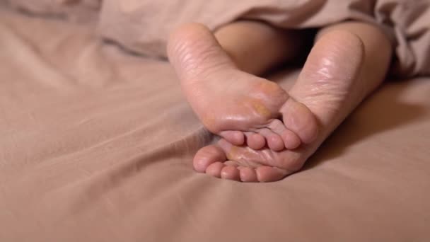 Női láb, repedések, bőrkeményedések a takaró alatt, ápolatlan sarok egészséges pihenés bőrkeményedés állapot hiba betegség, gomba sarok. Láb hidratáló lábgyógyász nő — Stock videók