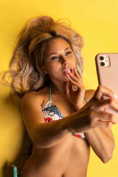 Fille prend selfie couché sur le sol dans un fond jaune dans un maillot de bain fille fond féminin beau jaune en utilisant la jeunesse, étudiant émotions adultes portant cool — Photo