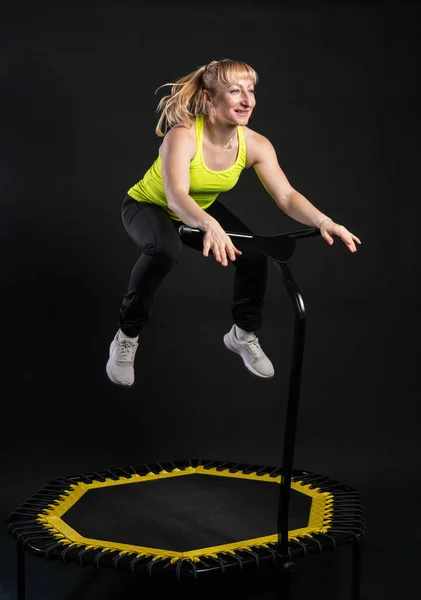 Dziewczyna na trampolinie fitness na czarnym tle w żółtym T-shircie skok trampoliny, aktywny fitness ciała skok stylu życia, cute bounce. młody instruktor mięśni cieszyć — Zdjęcie stockowe