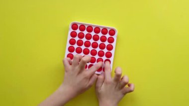 Sarı arka planda çocuk eğlencesi için popüler anti-stres oyuncağı. Renkli Fijit basit gamzeli popit oyuncaklarıyla çocuk üstten görüntüsü oynuyor. Stresli çocuklar. duyusal rotasyon eğitimi basit