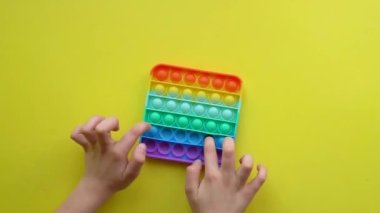 Sarı arka planda çocuk eğlencesi için popüler anti-stres oyuncağı renkli fijit basit popit popit silikon, moda duyusal renk itme rt, plastik trend şeklinde çocuk üst görünümü oynuyor. El.