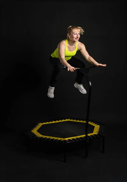 Mädchen auf einem Fitness-Trampolin vor schwarzem Hintergrund in einem gelben T-Shirt Energiesprung, Gerätebewegung, Sprungkraft. weiße Sportbekleidung Muskeltrainer genießen — Stockfoto