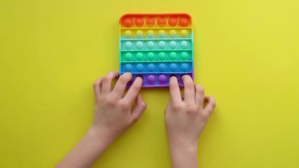Popit antistress leksak för barn underhållning på en gul bakgrund spelar ett barn ovanifrån i färgade fijit enkla dimple popit leksak silikon fidget, trendig pop push rt, slappna av gadget. Iew sensoriskt — Stockvideo