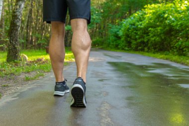 Spor ayakkabılarındaki bacaklar parka yakın koşuyor açık havada, ormanın etrafında, meşe ağaçları yeşil çimenler genç atletik spor ormanı, egzersiz bacakları parkı enerjisi esnetiyor.