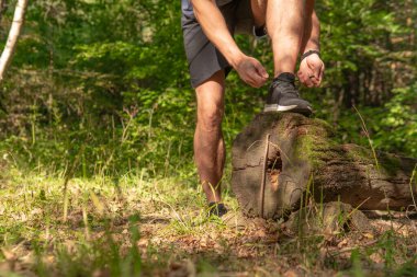 Sporcu, bacaklarının bağcıklarını spor ayakkabılarla bağlıyor. Parkta koşan sporcu, açık havada, ormanın etrafında koşuyor. Meşe ağaçları, yeşil çimenler genç sporcu sağlıklı koşucu.