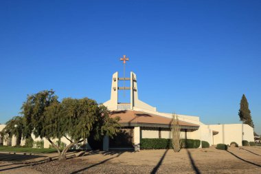 Phoenix, AZ - 5 Aralık 2025: Vadi Katolik Kilisesi 'nin ana binası kırmızı-turuncu ya da bakır tonlu haç ile kesişme noktasında elmas şekilli iki kulenin tepesine monte edilmiştir. 