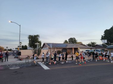 Phoenix, AZ - 13 Aralık 2025: Bir grup Phoenix kış maratonu destek ekibi, Paradise Lane ve 39. Cadde 'deki yerleşim yerlerinde serin kış sabahı koşuculara su ve içecek dağıtıyor.