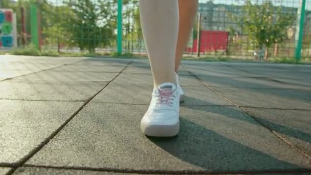 Primo piano di una donna gambe in scarpe da ginnastica a piedi lungo un campo o prato in campagna. — Video Stock