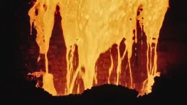 Dökümhanede bir kepçeden diğerine erimiş metal akışı. Fırında sıvı metal var. Sıvı metal üretim süreci. Endüstriyel fabrikada erimiş metal kalıbı. Yavaş çekim