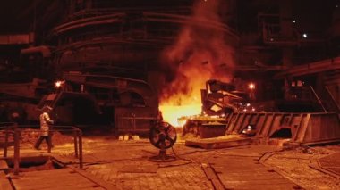 Dökümhanede bir kepçeden diğerine erimiş metal akışı. Fırında sıvı metal var. Sıvı metal üretim süreci. Endüstriyel fabrikada erimiş metal kalıbı. Yavaş çekim