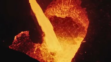 Dökümhanede bir kepçeden diğerine erimiş metal akışı. Fırında sıvı metal var. Sıvı metal üretim süreci. Endüstriyel fabrikada erimiş metal kalıbı. Yavaş çekim