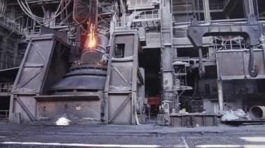 Dökümhanede bir kepçeden diğerine erimiş metal akışı. Fırında sıvı metal var. Sıvı metal üretim süreci. Endüstriyel fabrikada erimiş metal kalıbı. Yavaş çekim