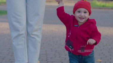 Anne küçük bir çocukla sokağa çıktı, kollarında onunla oynadı, çocuk ilk adımı attı ve yürümeyi öğrendi, mutlu bir aile, çocuk dünyayı öğrendi, Prores 422, bmpc4k.