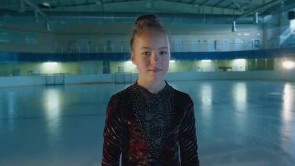 リンクの上に立つフィギュアスケートの女の子がカメラを見ていると、女の子はフィギュアスケートのために行くことを学ぶ。Prores422 — ストック動画